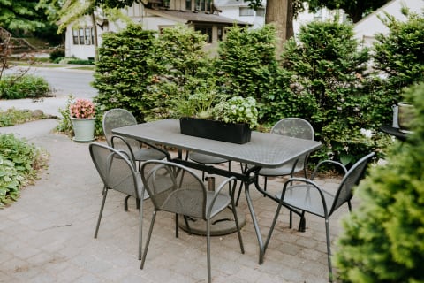 Outdoor patio with a metal table, chairs, and a planter filled with herbs.