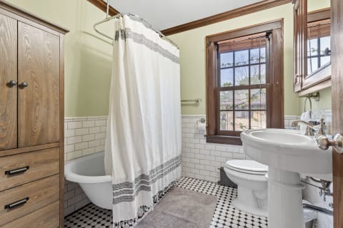 A vintage-inspired bathroom with a footed bathtub, wooden cabinet, and white shower curtain.