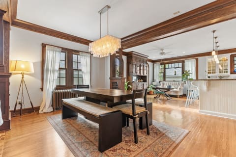Stylish dining area featuring a dark wooden table and elegant chandelier, with a view of the living space nearby.