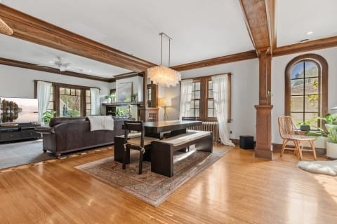 Interior view of a stylish living room and dining area with a leather sofa, a black dining table, and a chandelier.