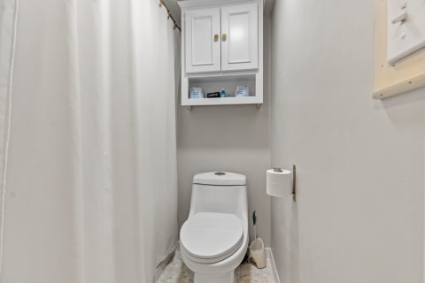 Interior view of a small bathroom with a white toilet, a cabinet above, and a shower curtain.