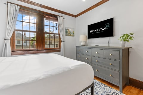 Cozy bedroom with a gray dresser, white bedding, and a large window.