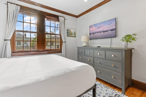 Modern bedroom featuring a window, white bedspread, gray dresser, and a television.