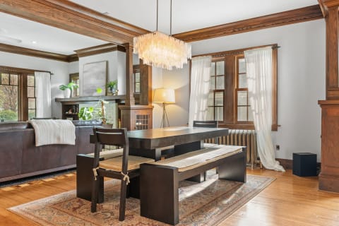 Cozy dining area with a wooden table, black chairs, and a modern chandelier, illuminated by sunlight.