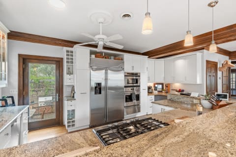 Modern kitchen featuring white cabinetry, granite countertops, and wooden ceiling beams.