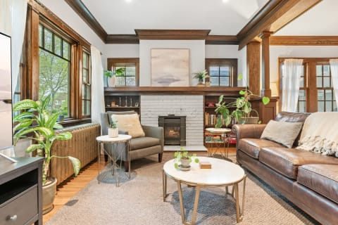 Cozy living room with brown leather sofa, grey armchair, and white-brick fireplace.