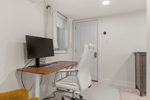 Minimalist home office with a white chair, wooden desk, and a monitor.