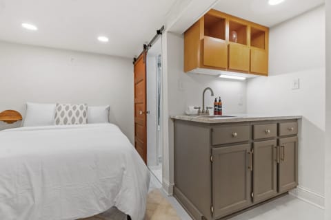 A modern studio featuring a bed with white linens and a kitchenette area.