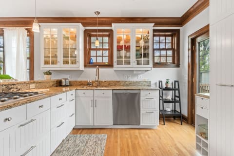A modern kitchen featuring white cabinetry, granite countertops, and large windows for natural light.