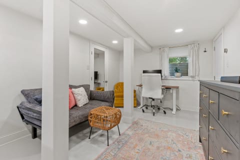 Cozy basement room with a gray sofa, workspace, and bright yellow accent chair.