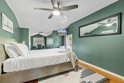 A contemporary bedroom with green walls, white bedding, and a cozy armchair by the window.