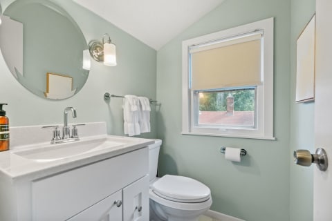 A small powder room featuring sage-green walls, a round mirror, and a marble countertop.