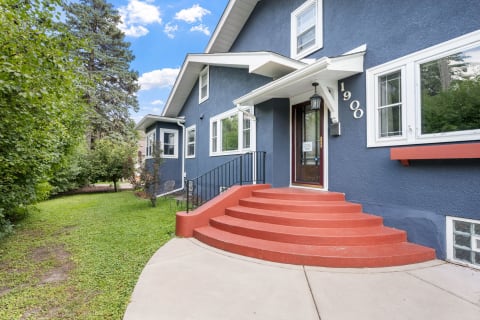 A blue craftsman-style home with coral steps, surrounded by green trees and shrubs.