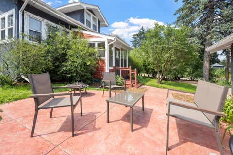 A cozy outdoor patio with modern seating and a glass table amidst lush gardens.
