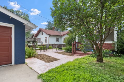 A peaceful neighborhood with a distinct blue garage, cozy outdoor seating, and well-kept gardens under a bright sky.