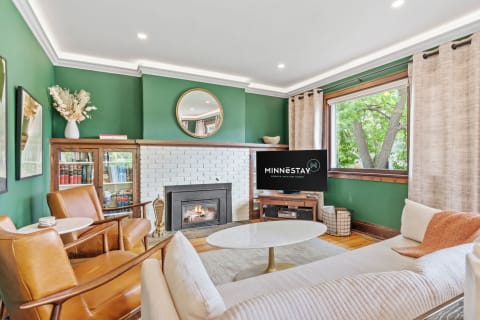 A stylish living room featuring green walls, a white fireplace, leather chairs, and a coffee table, creating a warm and inviting atmosphere.