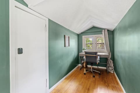 A small workspace with sage green walls, hardwood floors, a desk, and windows letting in natural light.