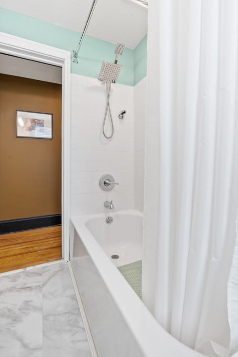 Modern bathroom with tub-shower combo, rainfall showerhead, and marble floor.