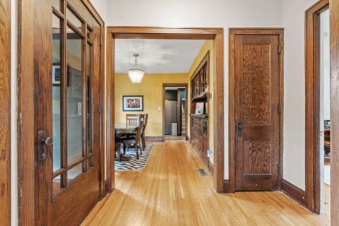 A wooden hallway leading to a dining area with hardwood floors and framed artwork on the walls.