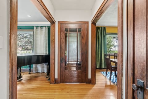 A wooden entryway leading to a living area with hardwood floors and a black grand piano.