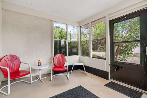 Screened porch with red chairs and a white table, surrounded by greenery.