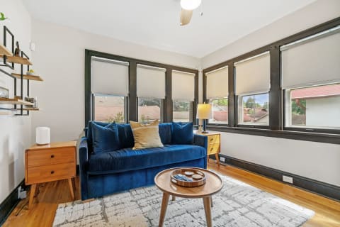 Bright living room featuring a blue velvet sofa, wooden accessories, and large windows.