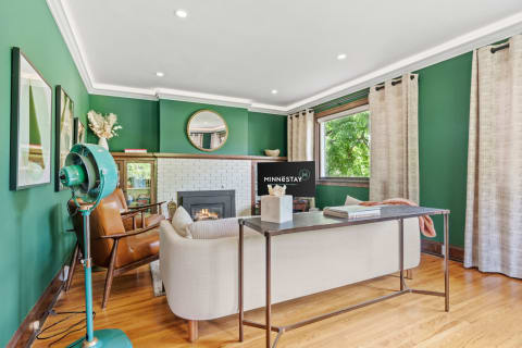 A living room with green walls, a fireplace, beige curtains, and stylish furniture.