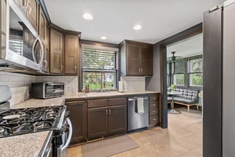 A modern kitchen with dark wood cabinets, granite counters, stainless steel appliances, and a cozy dining nook with black leather seating.