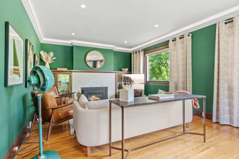 Stylish living room with green walls, cozy furniture, and natural light from windows.