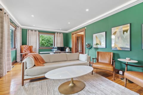 A cozy living room featuring green walls, a beige sofa with an orange throw, leather armchairs, and modern decor.