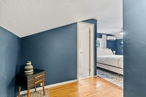 Cozy bedroom entrance with navy walls, wooden floor, and black nightstand with a vase.