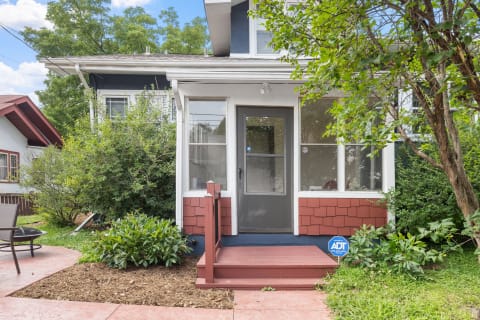 A welcoming cottage with a red porch, navy blue exterior, and lush greenery.