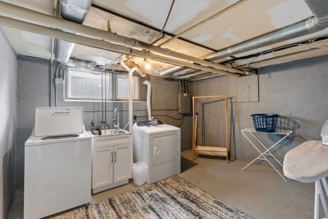 Basement laundry room with washing machine, dryer, sink, and drying rack.