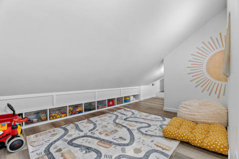 An inviting attic playroom featuring a colorful rug, toy storage, and a sun mural.