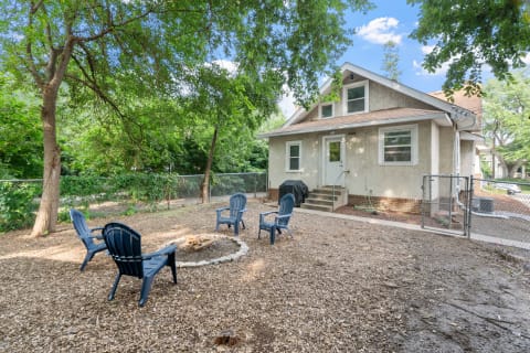 A house with a backyard featuring a fire pit and blue chairs.