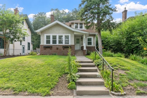 Facade of a two-story house with a lawn and steps leading to the entrance.