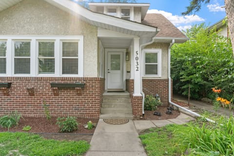 A residential house with a brick and stucco exterior, featuring a front porch and colorful flower beds.