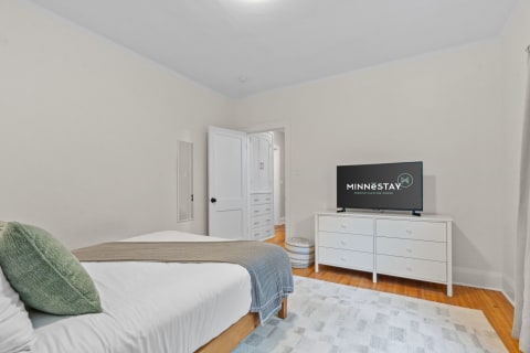 A bright and cozy bedroom with a bed, dresser, and television.