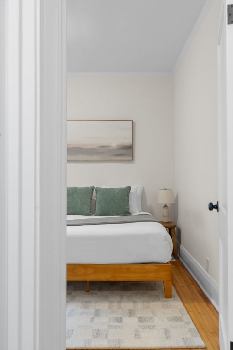 A cozy bedroom featuring a made bed with green pillows and a wooden nightstand.