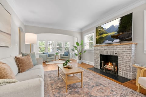 A bright living room featuring a sofa, fireplace, and a flat-screen TV displaying a landscape image.