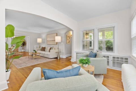 A stylish living room featuring two green armchairs, a beige couch, and large windows.