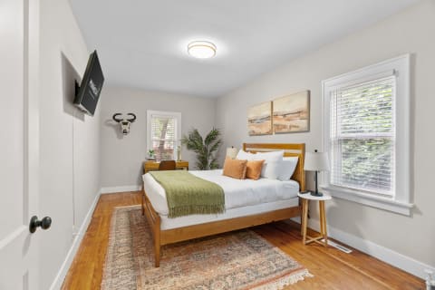 Cozy bedroom featuring a wooden bed, decorative pillows, and wall-mounted TV.