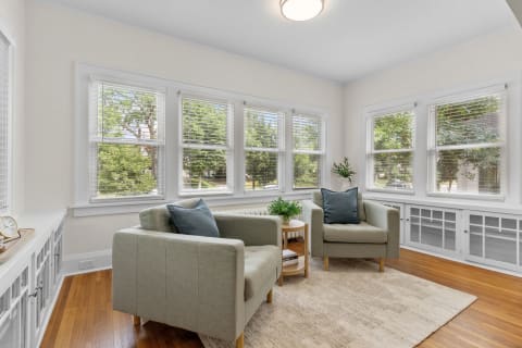 Cozy sunroom featuring two green armchairs, natural light, and plants.