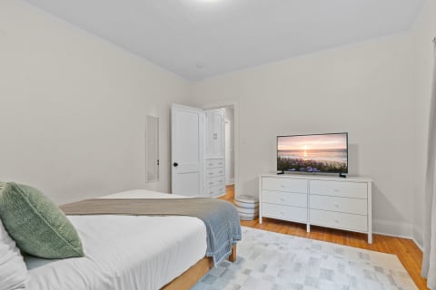 Cozy bedroom with a bed, white dresser, and a television displaying a sunset.