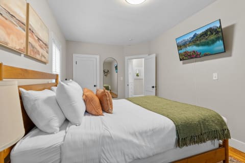 Modern bedroom featuring a wood bed with white bedding and pillows, abstract wall art, and a flat-screen TV.