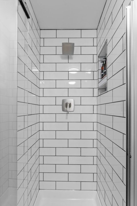 Interior of a white tiled shower with metal showerhead and built-in shelf.