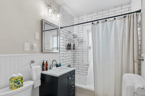 Interior view of a modern bathroom with subway tiles, a black vanity, and a shower curtain.