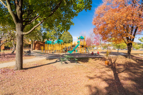 Colorful playground with autumn foliage, picnic table, and blue sky.
