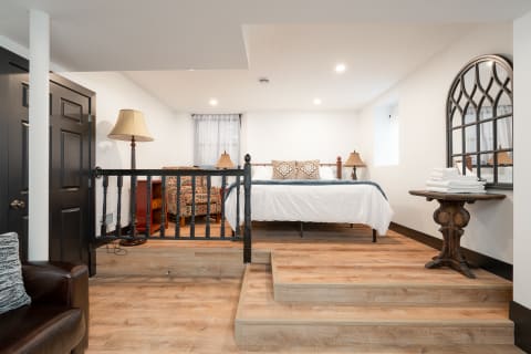 A modern basement bedroom with a bed, patterned chairs, and a stylish mirror.