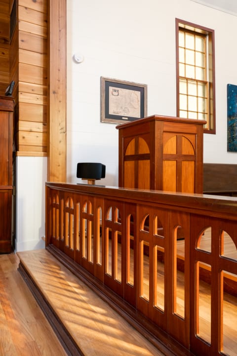 Interior of a wooden hall with a railing, podium, lamp, and artwork.
